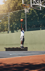 Image showing Basketball, jump and athlete scoring a goal during a match or training on an outdoor court. Fitness, sports and man jumping to dunk while playing a game or doing a exercise on a basketball court.