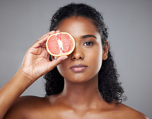 Image showing Woman, face skincare or grapefruit for glow, relax wellness health or exfoliate facial on grey studio background. Portrait, Indian beauty model and vitamin c food product in hands for anti aging eyes