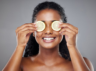 Image showing Skincare, portrait and woman with lemon on her eyes for health, beauty and wellness standing in a studio. Happy, smile and face of girl model from Brazil with citrus fruit isolated by gray background