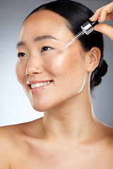 Image showing Skincare, face oil and woman with wellness for her skin against a grey studio background. Happy, smile and young Asian model with a facial serum for body healthy, dermatology and a beauty glow