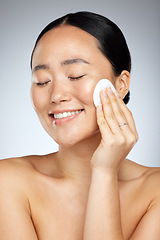 Image showing Skincare, asian and woman cleaning face with soft cotton pad for healthy and fresh skin routine. Hygiene, natural and beauty of girl with cosmetics removal swab on grey studio background.