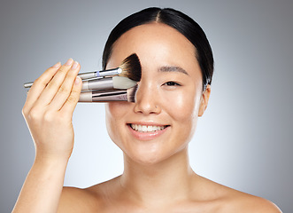 Image showing Beauty, makeup and woman with brush for cosmetics against a grey mockup studio background. Portrait of a young, happy and Asian model with a product for facial cosmetic care and mock up space