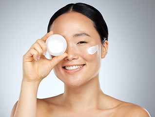 Image showing Cream, eye skincare and woman with natural wellness product against grey mockup studio background. Portrait of happy asian beauty model smile with pot of facial lotion with mock up space