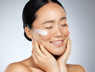 Image showing Skincare, beauty and woman with smile using dermatology face cream or cosmetics against studio background. Face of happy, healthy and Asian model doing facial care for wellness and health of skin