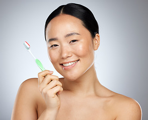 Image showing Beauty, dental care and oral hygiene with an asian woman in studio on a gray background with a smile. Portratit, teeth and toothbrush with a young female brushing her teeth for health or wellness