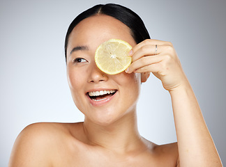 Image showing Portrait, happy and woman using lemon for facial skincare cleaning, vitamin c and cosmetic benefits in studio in Tokyo. Smile, fruit and young Asian beauty model cleaning a glowing face for wellness