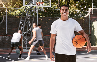 Image showing Portrait of african man, basketball and athlete on basketball court outdoors. Basketball player, fitness and healthy sports training on court in urban city with teammates playing in background