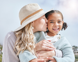 Image showing Mother kiss, girl and happy face of a mama and child adoption happiness outdoor for mothers day. Portrait of a hug and love smile of a kid in the summer sun embracing the sunshine in nature