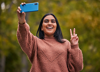 Image showing Selfie, park and young woman, peace and smartphone, pose while outdoor in nature and happy. Gen Z person from India, smile and technology, fun and youth, walking outside in garden with hand gesture.