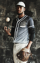 Image showing Baseball, sports and uniform with a man athlete on a dark background wearing a mitt while holding a ball. Portrait, sport and confident with a male baseball player standing against a dugout wall