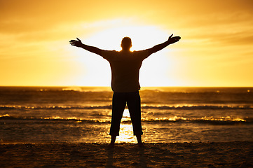 Image showing Beach, sunset and silhouette of man in nature with arms to the sky carefree while on vacation. Freedom, shadow and guy standing outdoor by sea or ocean on holiday, adventure or journey in Australia.