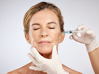 Image showing Needle, surgery and face with mature woman getting an injection in her cheek for beauty, skincare and medicine in studio on a blue background. Filler, product and cosmetics with a female model inside