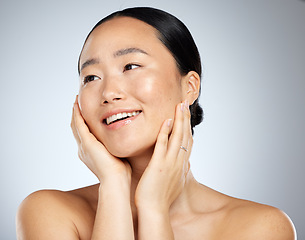 Image showing Asian woman, face glow and skincare routine with hands touching cheeks on grey studio background. Smile, happy or beauty model in healthy wellness, relax self love dermatology or hydrated skin facial