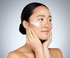 Image showing Cream, skincare and woman with product for face against a grey studio background. Thinking, wellness and Asian model with facial lotion, creme or sunscreen with idea for health and clean body