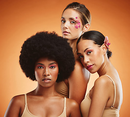 Image showing Makeup, women and beauty, diversity and flowers on orange studio background. Models, skincare and friends together with serious facial expression, organic cosmetics or empowerment with floral orchids