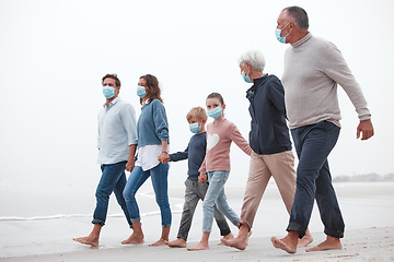 Image showing Covid, mask and big family walking together on a beach with mother, father and children outdoor. Parents, kids and grandparents walking on sand at the ocean water waves holding hands with love