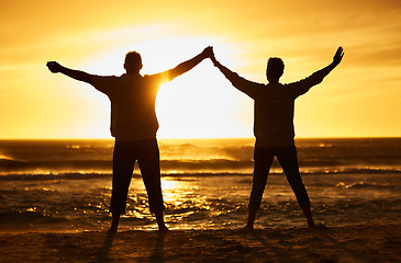 Image showing Beach, sunset and silhouette of a couple with freedom on adventure, journey or travel vacation together. Carefree, nature and people enjoying their outdoor holiday at the ocean or sea in the evening.