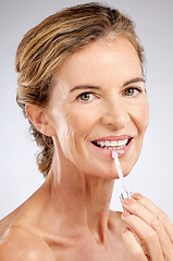 Image showing Cosmetics, lip gloss and senior woman for wellness, natural beauty and healthy with grey studio background. Portrait, makeup and elderly female with smile, confident and happy with hydrate product.