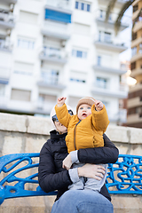 Image showing Young mother with her cute infant baby boy child on bench in city park.