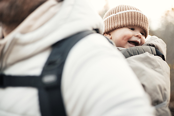 Image showing Sporty father carrying his infant son wearing winter jumpsuit and cap in backpack carrier hiking in autumn forest.