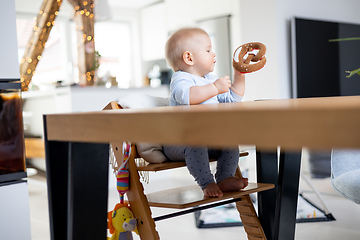 Image showing Happy infant sitting at dining table and playing with his toy in traditional scandinavian designer wooden high chair in modern bright atic home. Cute baby playing with toys