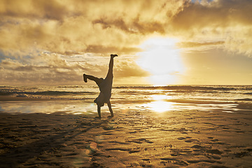 Image showing Sunset, silhouette and child doing cartwheel at the beach having fun, playing and enjoy nature. Freedom, inspiration for youth and kid doing handstand by ocean on summer vacation, holiday and weekend