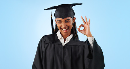 Image showing Woman, ok sign and smile for graduation in studio with review with vote, choice or support by blue background. Student girl, portrait and celebration for icon, emoji or decision for success with goal