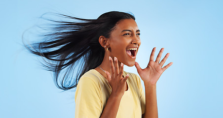 Image showing Woman, scream and wind for hair in studio for mock up on blue background with good news. Indian person, happy and smile in excitement for winning with success, celebration or announcement in space