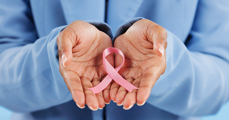 Image showing Hands, pink ribbon and breast cancer support with awareness and healthcare icon on blue background. Person in studio, medical symbol and wellness with care, trust and kindness in solidarity campaign