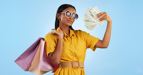 Image showing Woman, shopping bag and money fan, wealth and commerce with customer in sunglasses on blue background. Cash, financial freedom and retail, fashion and product choice, rich and shop discount in studio