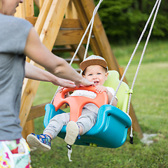 Image showing Mother pushing her infant baby boy child on a swing on playground outdoors.