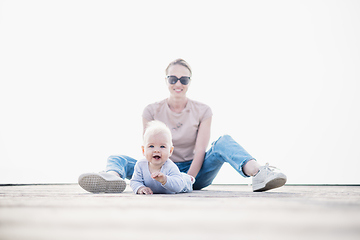 Image showing Happy family. Young mother playing with her baby boy infant oudoors on sunny autumn day. Portrait of mom and little son on wooden platform by lake. Positive human emotions, feelings, joy.