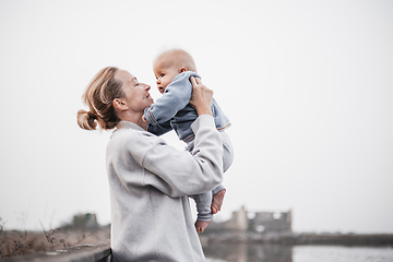 Image showing Tender woman caressing her little baby boy infant child outdoors on autumn trip to Secovlje salinas landscape park, Slovenia. Mother's unconditional love for her child.