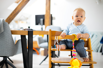 Image showing Happy infant sitting and playing with his toy in traditional scandinavian designer wooden high chair in modern bright atic home. Cute baby.