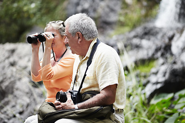 Image showing Senior, couple and binocular in forest for tourist, sightseeing or vacation with waterfall and scenery. Elderly, man and woman in woods or nature for holiday, adventure or experience with backpack