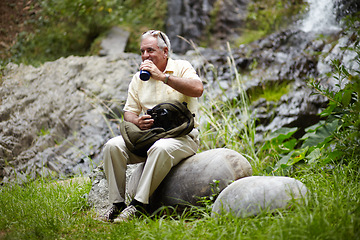 Image showing Senior, man and drinking water in forest for break, sightseeing or vacation with waterfall and scenery. Elderly person in woods or nature to rest on holiday, adventure or experience with backpack