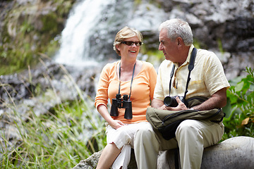 Image showing Senior, man and woman with binocular for travel, sightseeing or holiday with happiness on rocks. Elderly, couple and face with smile for waterfall, vacation and adventure on retirement or tourism