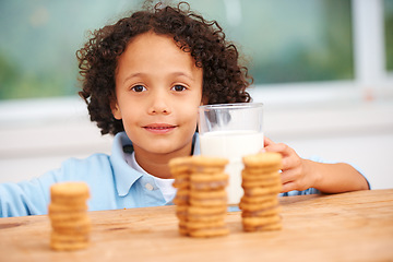 Image showing Milk, cookies and portrait of boy child by the kitchen counter eating a sweet snack or treat at home. Smile, dessert and hungry young kid enjoying biscuits by a wooden table in a modern family house.