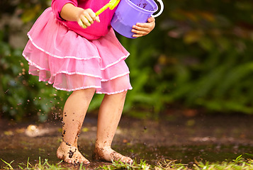 Image showing Legs, girl and kid with toy bucket in muddy puddle for play, explore and child development in garden or backyard. Person, feet or toys in mud water for activity, playing and freedom outdoor in nature