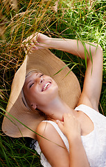 Image showing Grass, hat and woman relax on lawn with peace, happiness and freedom in summer. Outdoor, fashion and girl lying in field with smile on face for holiday, vacation or free time in nature with wellness