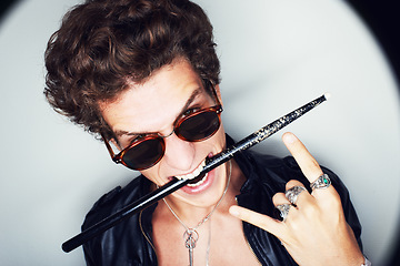 Image showing Rock man, horns and studio portrait with drumstick, sunglasses or biting in spotlight by white background. Punk musician, drummer or artist with emoji, icon and hand sign for performance at concert