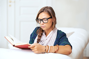 Image showing Thinking, reading and woman on sofa with book, knowledge and learning with literature in home. Relax, paperback and studying in apartment, girl in glasses on couch with story journal in living room.