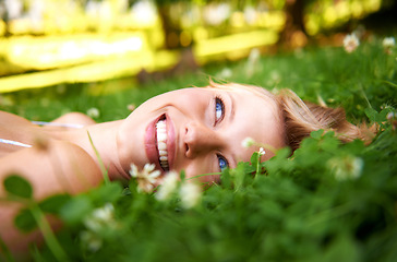 Image showing Spring, happy and calm with woman on grass in nature for relax, smile and peace. Park, flowers and field with face of female person lying in countryside meadow for summer, vacation and wellness