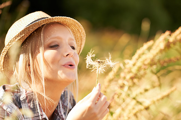 Image showing Woman, blow flower and wish in nature with smile, wheat and grain in field, fun and playful in outdoors. Happy female person, freedom and fashion or hat, peace and joy on countryside vacation or trip