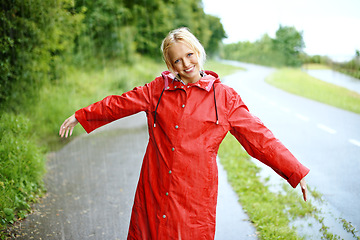 Image showing Woman, smile and raincoat in rain with arms, wet and cold from weather, winter and nature. Happy female person, fashion and red jacket in storm, rainfall and protection from water, face and outdoors