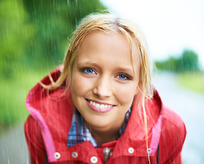 Image showing Woman, smile and raincoat in nature rainfall, wet and cold from rain, weather and outdoors. Happy person, fashion and red coat in portrait, storm and protection from water, vacation and travel