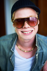 Image showing Smile, cool and portrait of a man with sunglasses for fashion, streetwear and a teen trend. Happy, young and face or a person with trendy, stylish or fashionable eyewear, funky cap or shades