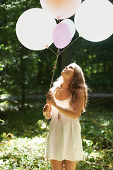 Image showing Woman, holding balloons and peace in nature, playful and outdoors in forest, party decor and celebrate for freedom. Female person, sunshine and birthday in park, milestone and achievement for growth