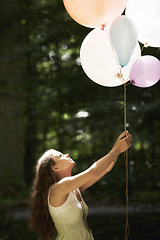 Image showing Woman, holding balloons and fun in nature, playful and outdoors in forest, party decor and celebration for freedom. Female person, sunshine and birthday in park, milestone and achievement for growth