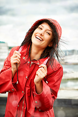 Image showing Woman, smile and raincoat in portrait outdoors, storm and cold on holiday, travel and weather. Female person, happy and winter on vacation, outside and positive on rooftop, rainfall and insurance